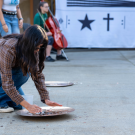 A student kneels on the ground, throwing pennies in a cymbal, while others observe nearby.